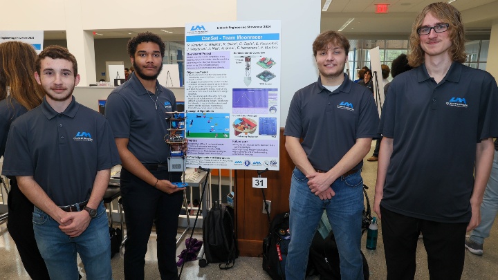 A group of male students from The University of Alabama in Huntsville standing next to a research poster.