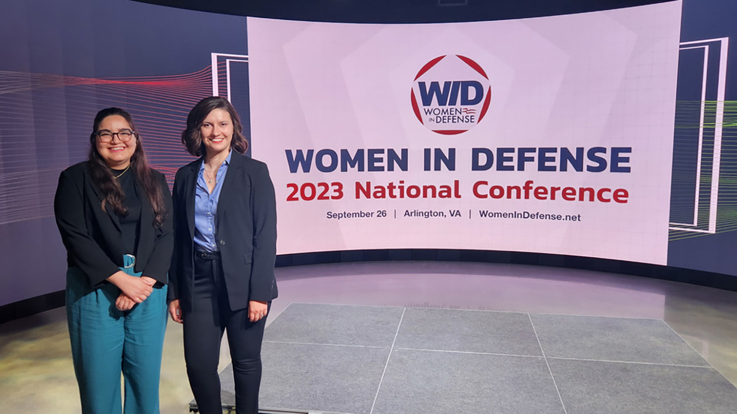 two women pose next to a Women in Defense banner