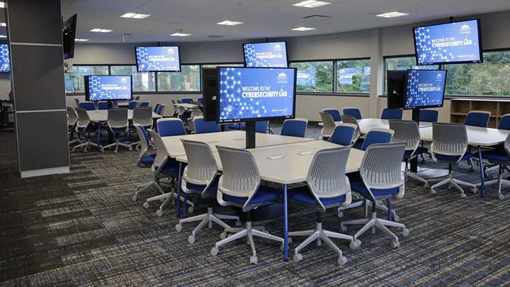 The New College of Business Cybersecurity Lab featuring several large tables and seating and tv screens.