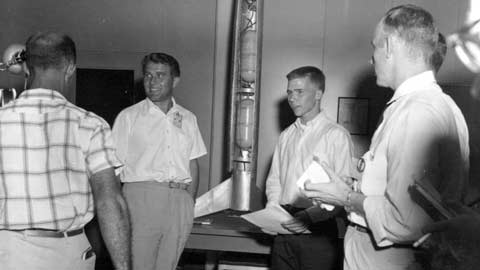 Dr. Wernher von Braun and 17-year-old Jimmy Blackmon flank his rocket creation on Redstone Arsenal