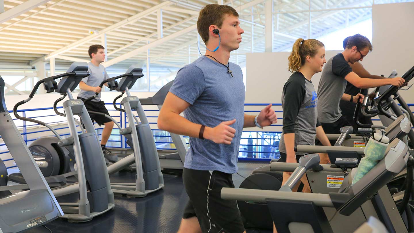 a man (left), woman (middle), and man (right); all on treadmills exercising in a fitness center.