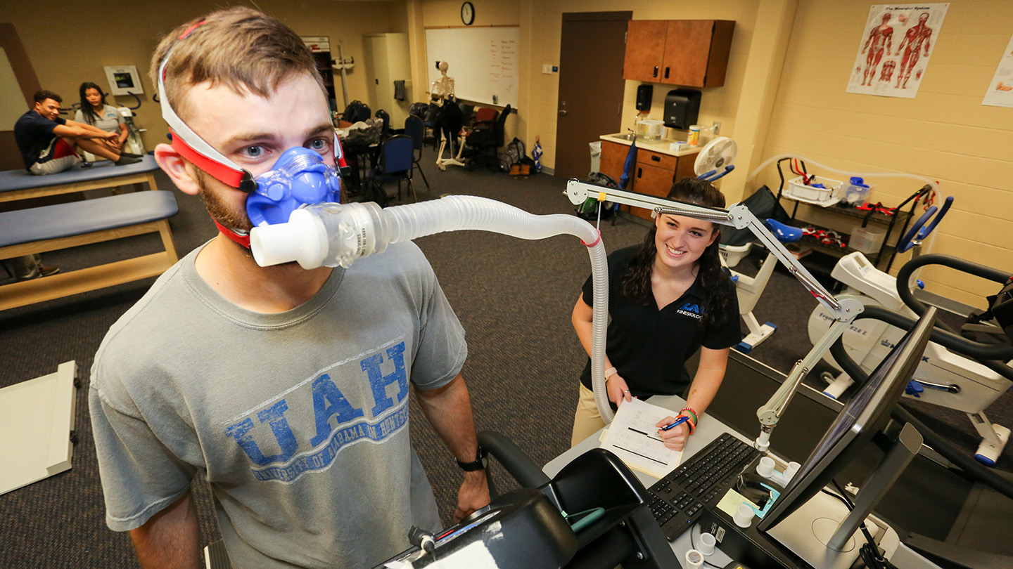 student wearing an oxygen breathing mask while another student makes observations