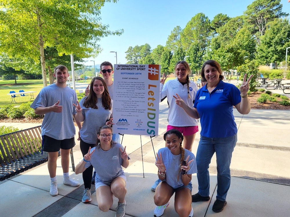 SFM Club members and advisor posing in front of an event poster