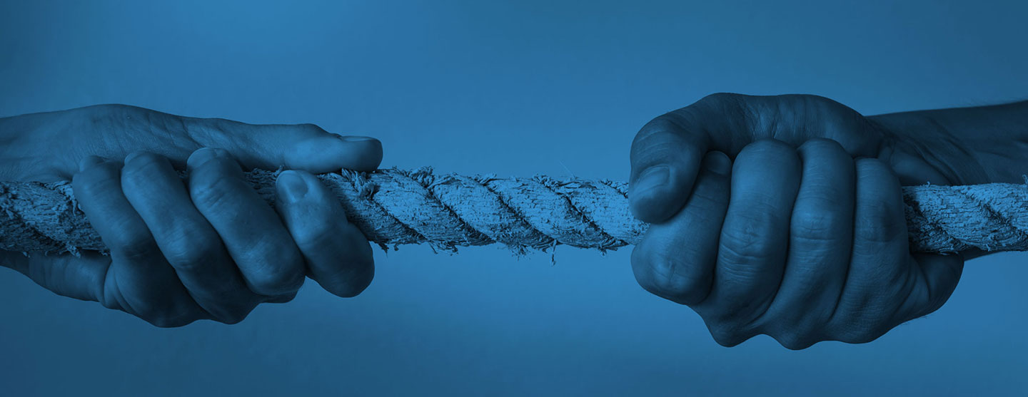 Close-up of two hands gripping opposite ends of a thick rope, pulling in opposite directions against a solid blue background, symbolizing tension or conflict.