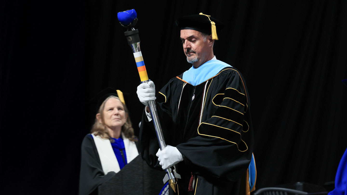 Doctor David Kyle carries U A H's ceremonial mace at a graduation ceremony in 2025.