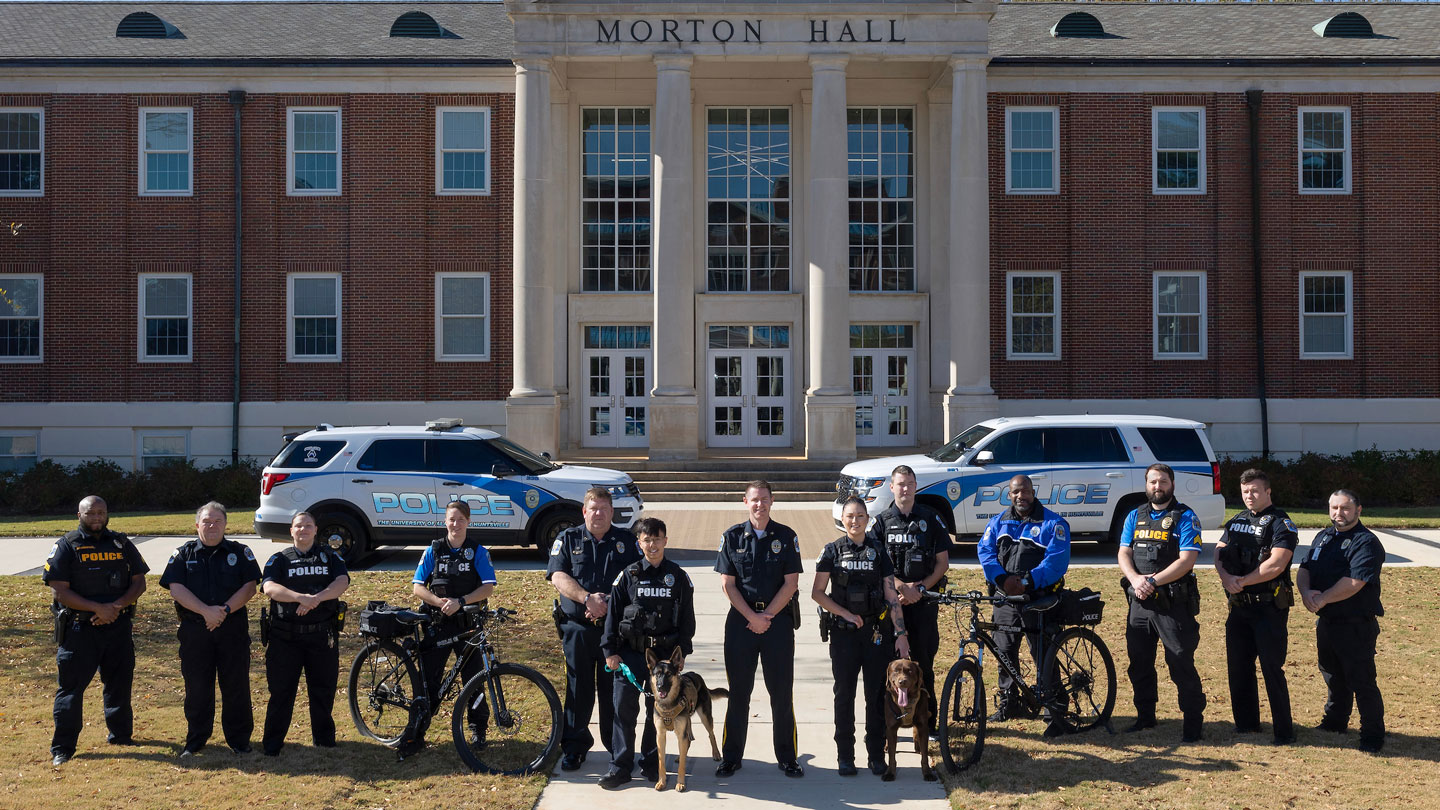 the campus police department of U A H pose for a group photo with patrol cars and assistance dogs in front of Morton Hall