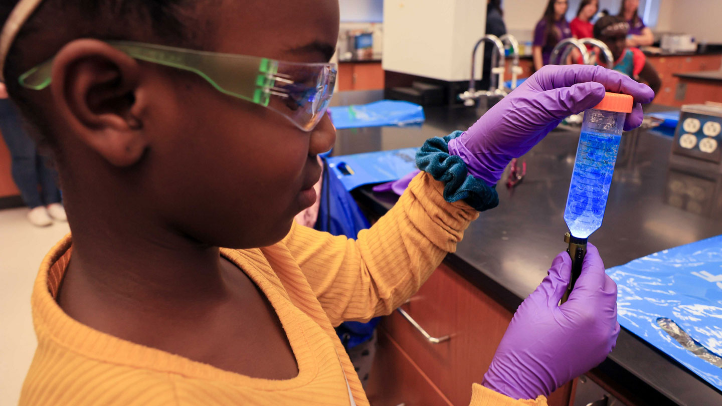A child examines a test tube while wearing safety glasses