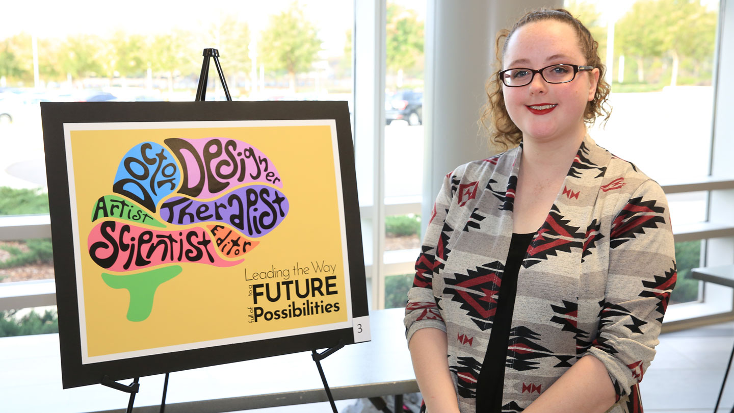 A proud student stands next to their creative graphic of a brain made up of words representing career paths