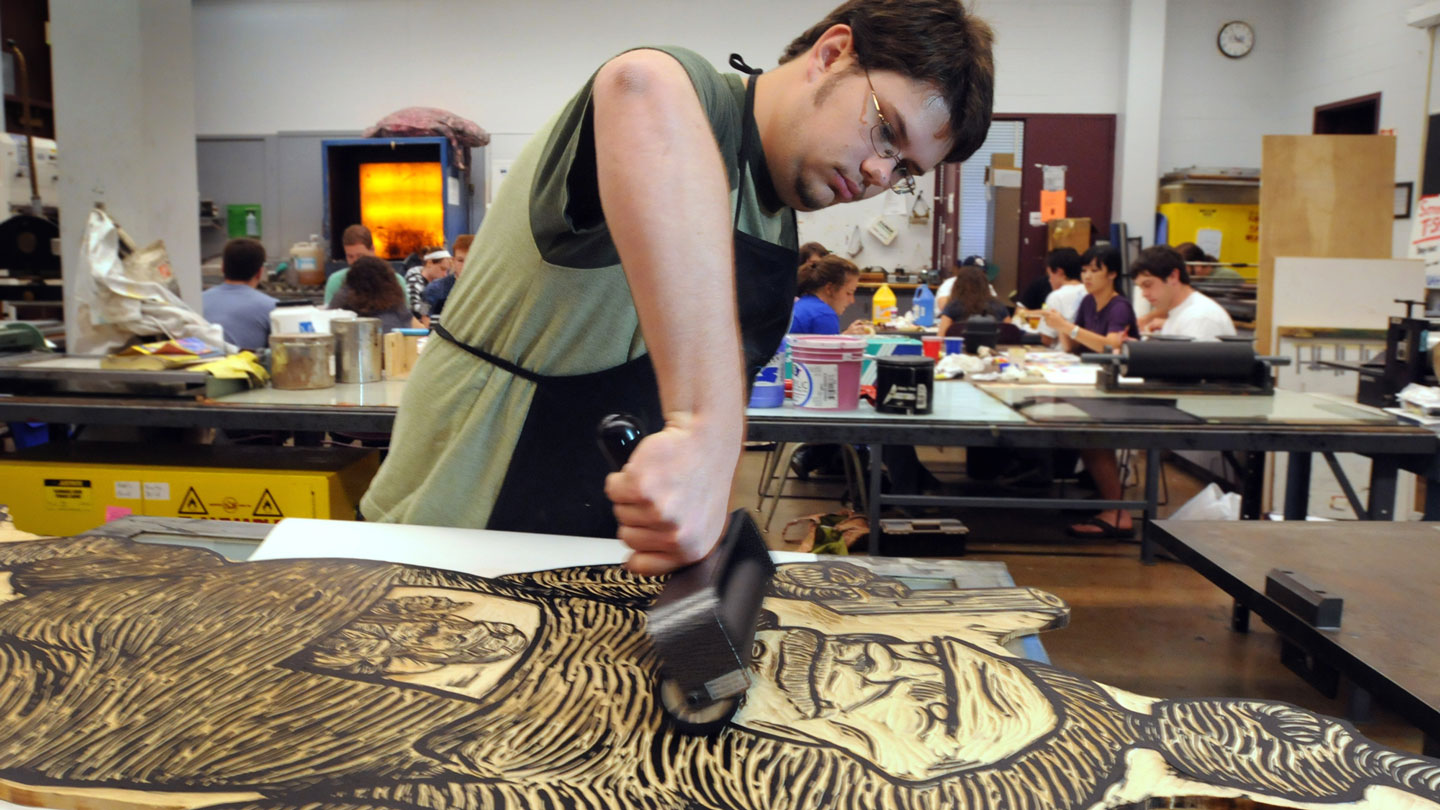 A student uses a roller to apply ink for printmaking