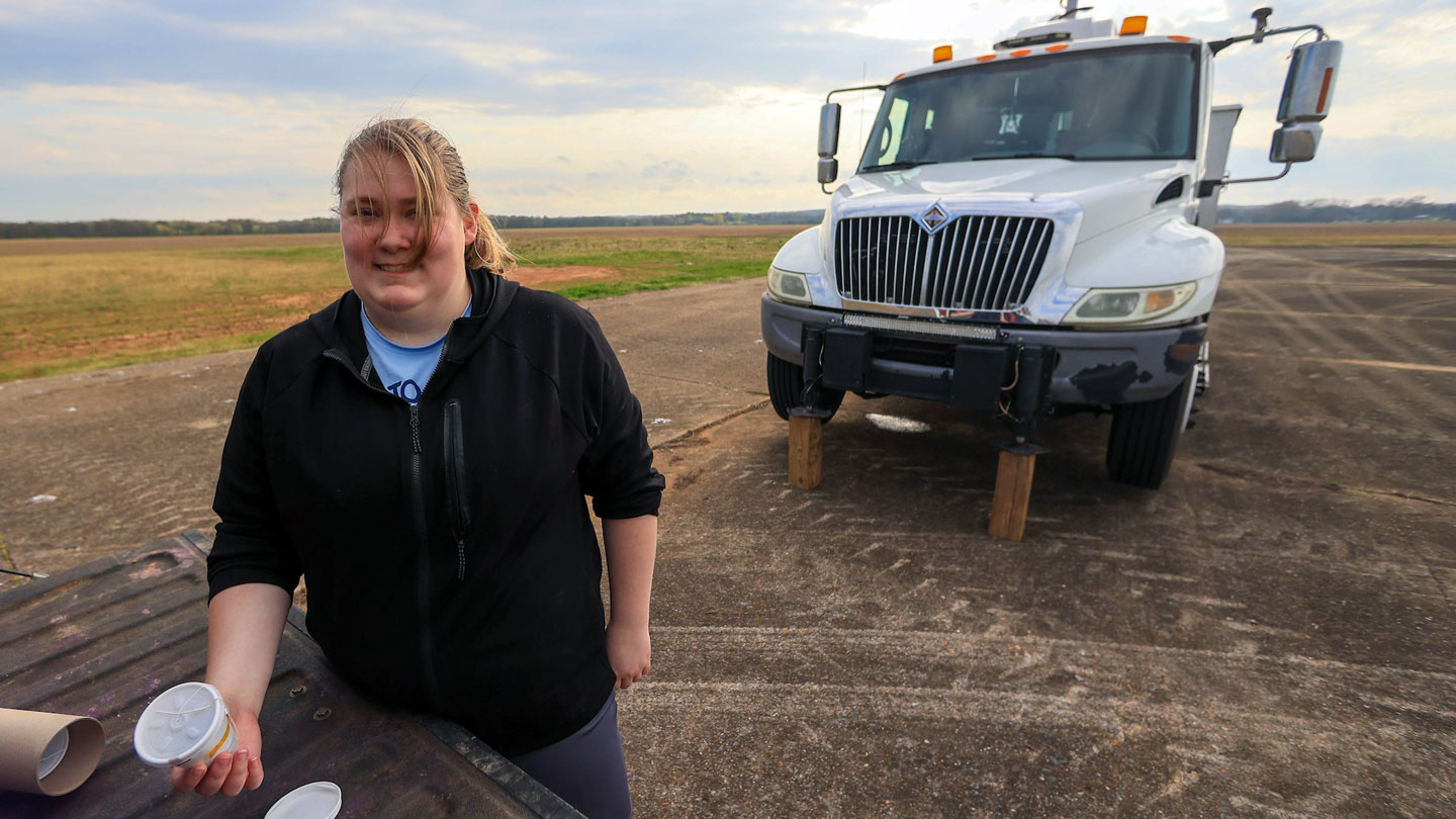 A student stands in front of a truck full of weather tracking equipment.