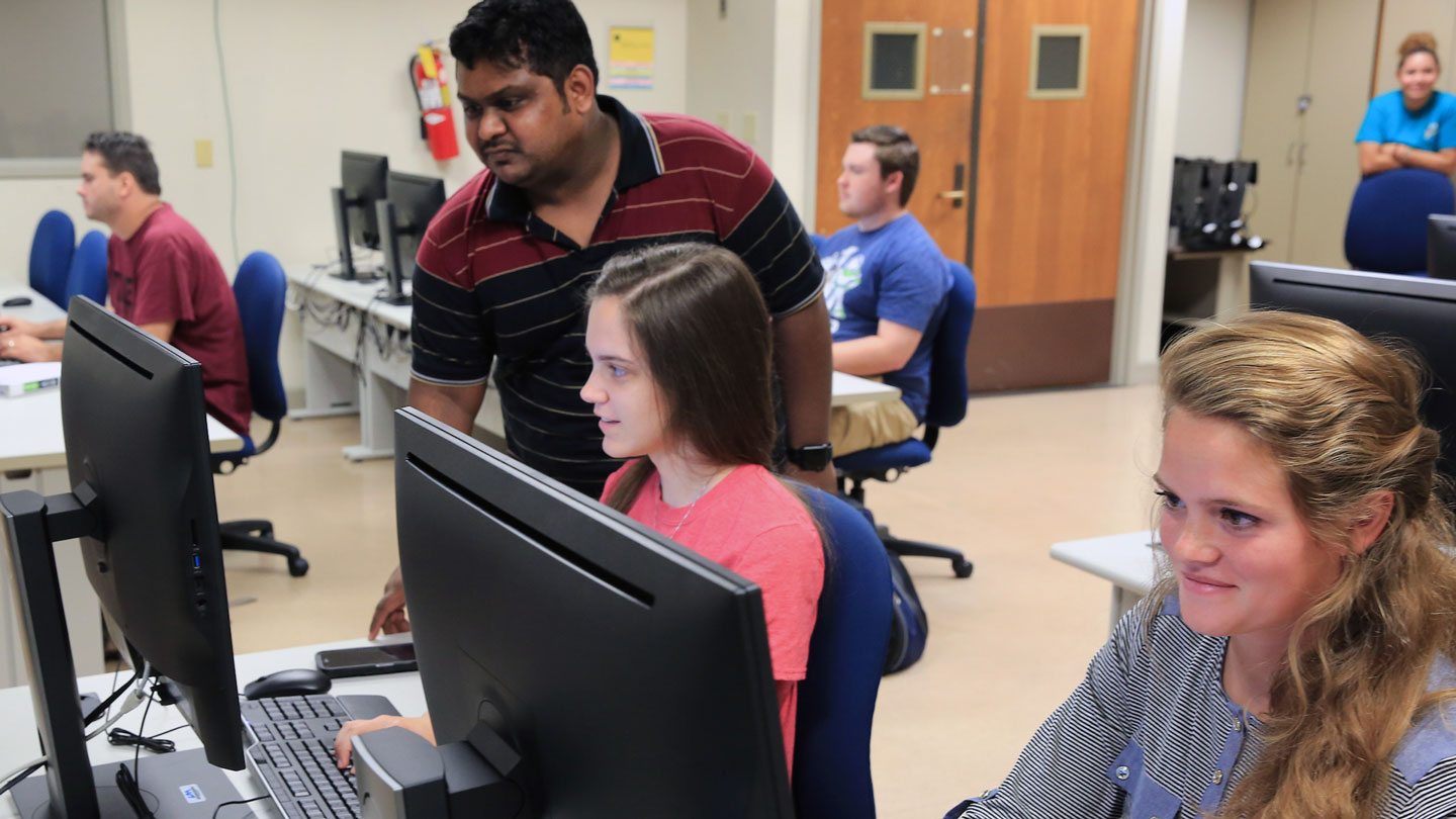A student looks over another students work on their computer