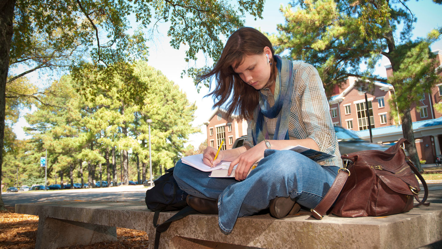 A student peacefully writes while sitting on campus