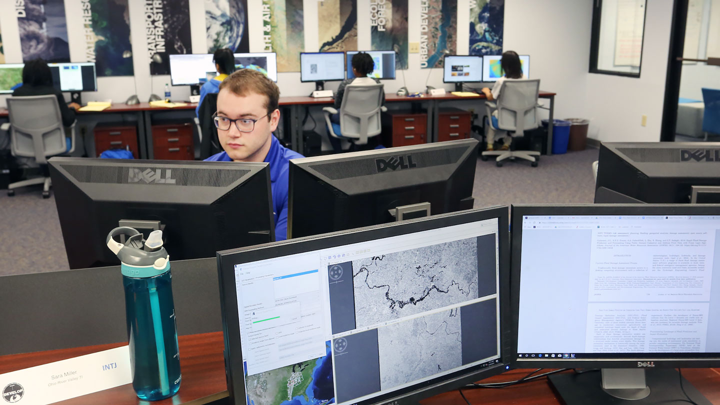 A man uses a multi monitor computer to work on a earth systems lab