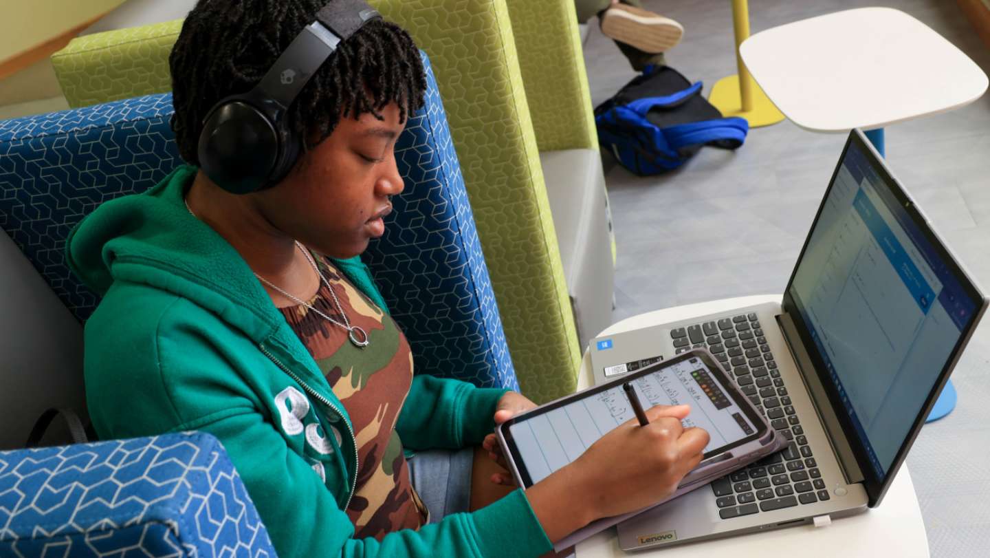 Woman sitting in a chair working on her laptop while wearing headphones.