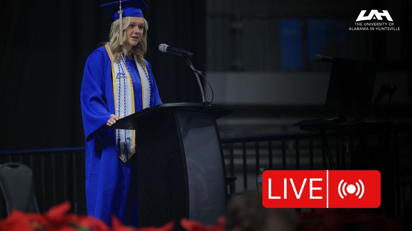 A woman in blue graduation regalia speaks to her graduating class
