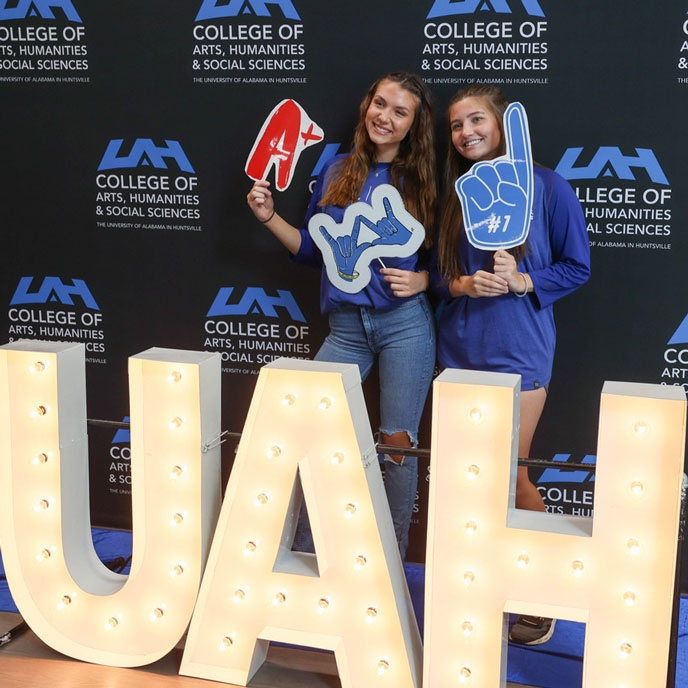 smiling UAH students pose in front of an illuminated UAH sign