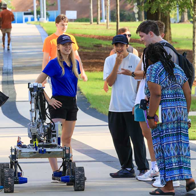 Students talkiing while standing on walkway that passes through a greenway.