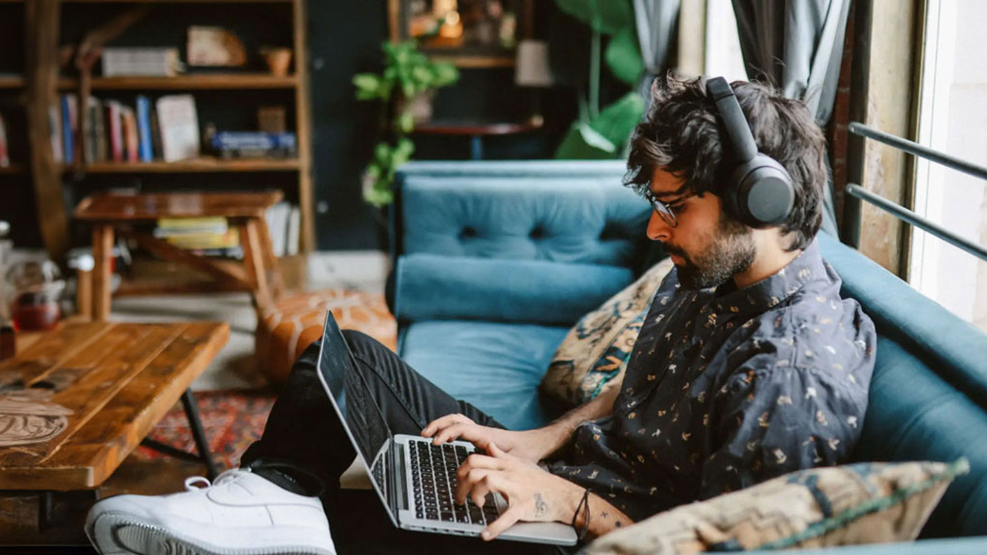 a student wearing headphones works diligently on his laptop in his apartment