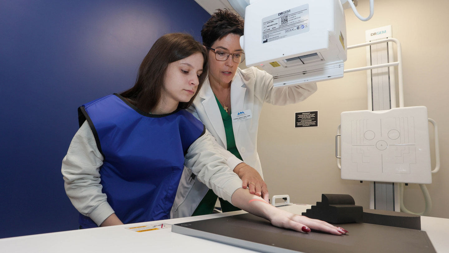 A UAH nurse practitioner gently places a student's hand beneath an x-ray machine.