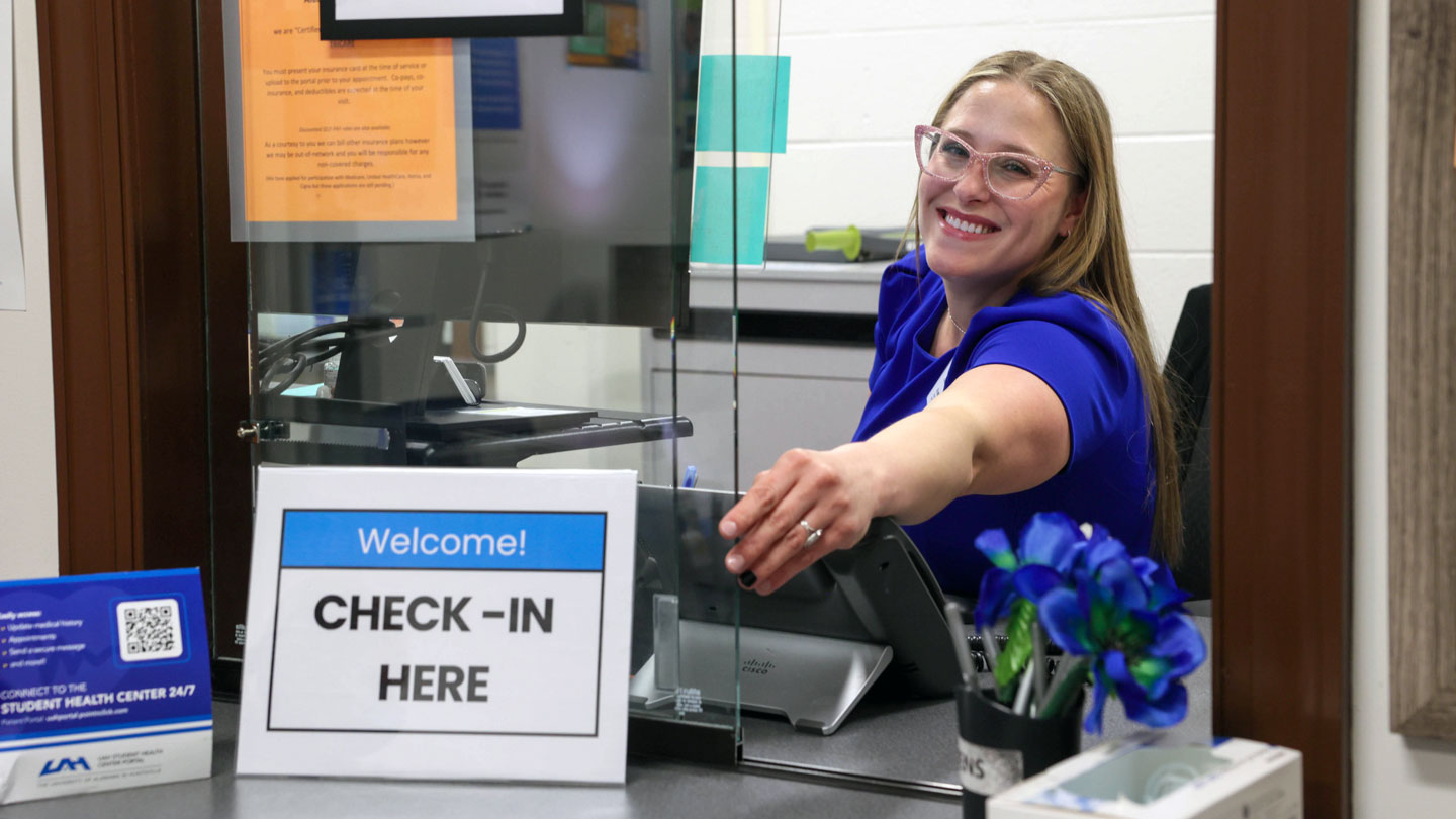 A smiling UAH clinic staff member greets you at the check-in counter.