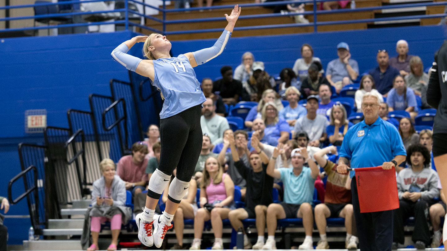 A UAH volleyball player jumps to serve at a game in front of a crowd of fans.