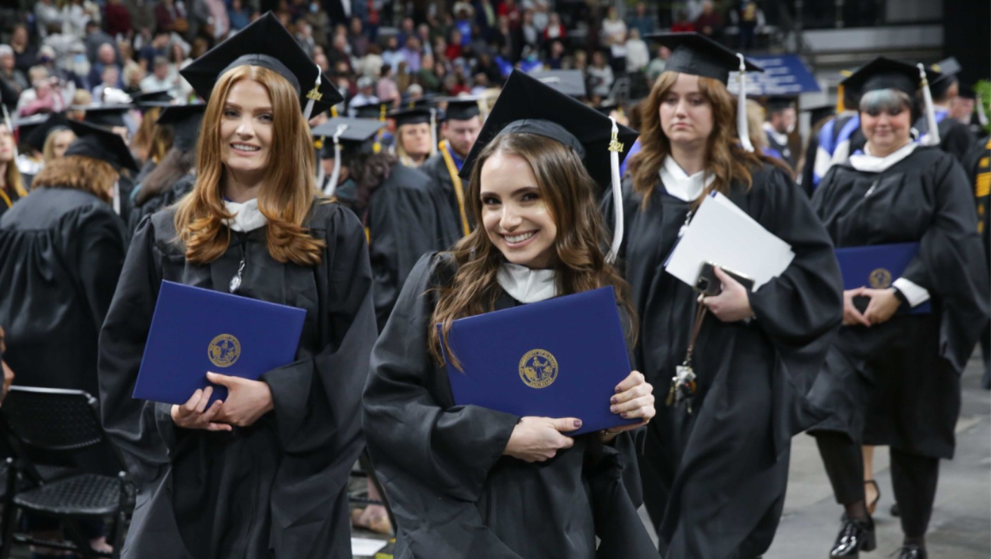 Students at graduation walking, holding deplomas.