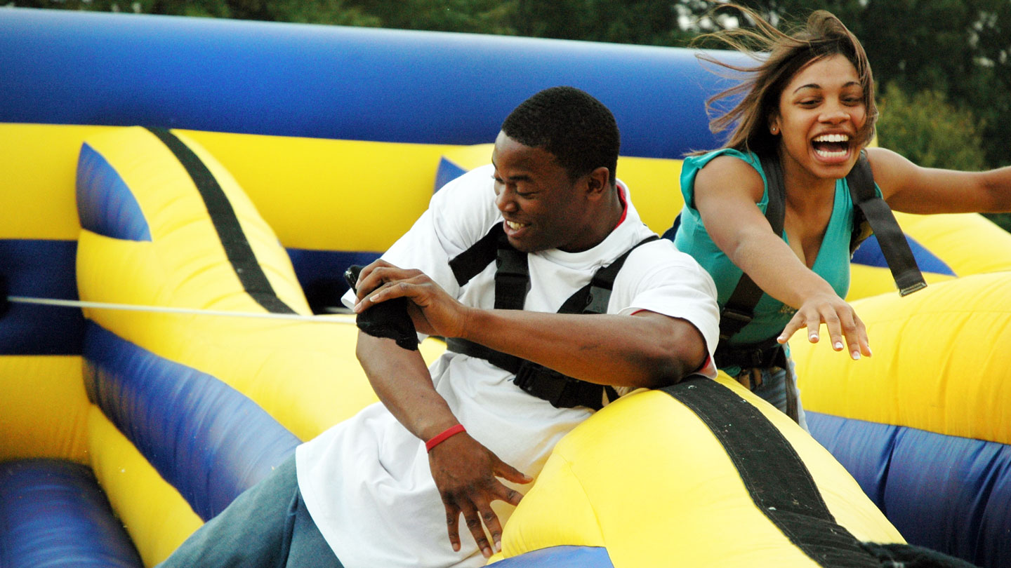 Two U A H students tethered together by a harness laugh as they fall down during a  obstacle course race.