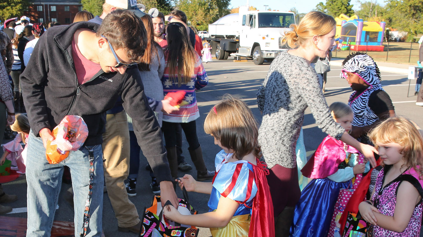 A student government association member gives candy to a young girl in a Snow White Halloween costume.