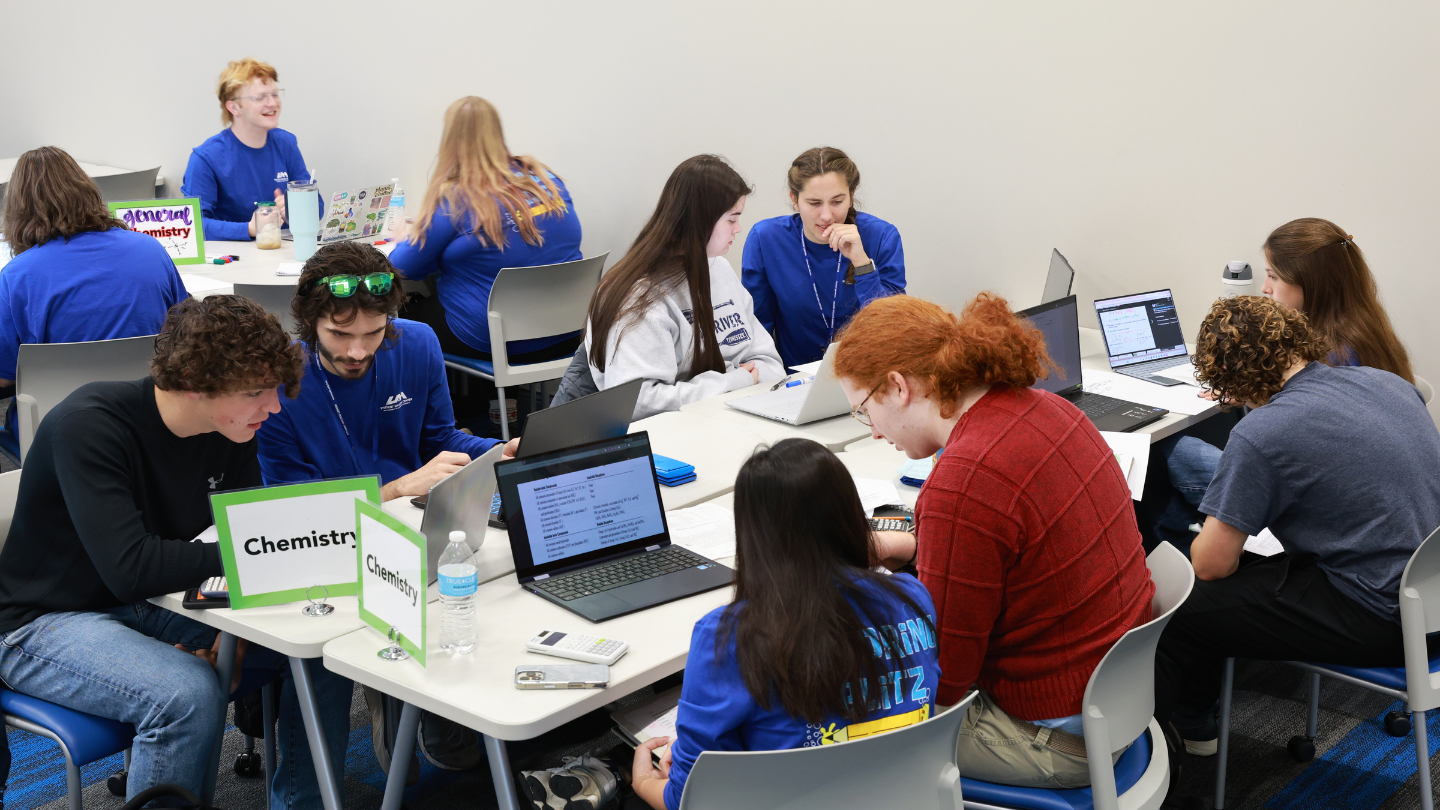 UAH students in a classroom work collaboratively in groups on chemistry assignments using laptops and calculators.