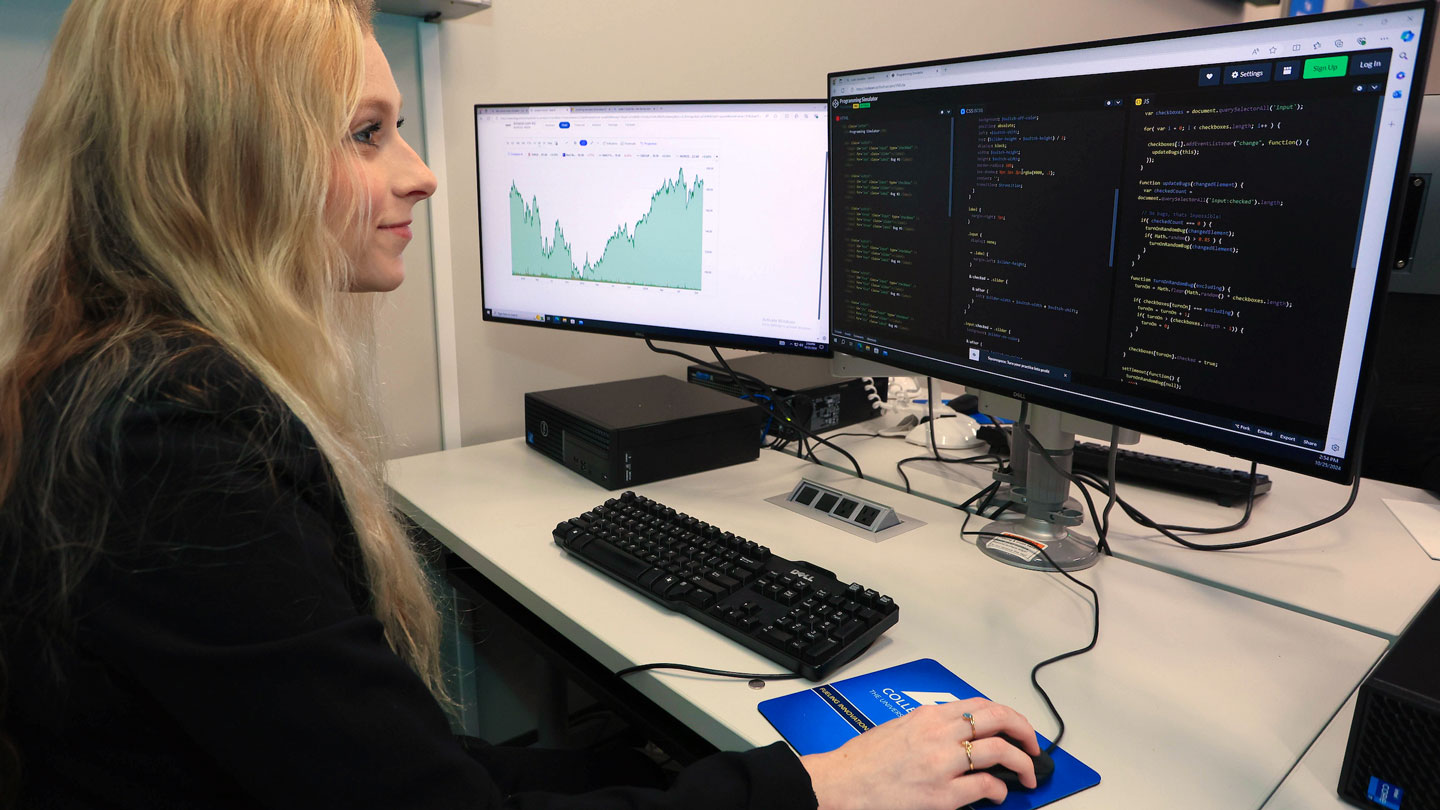 a U A H business student in business attire studies cybersecurity on her desktop computer.