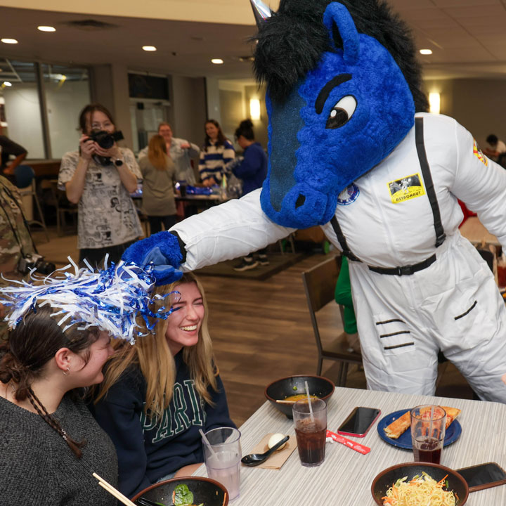The UAH mascot waves a pom-pom at two laughing students.