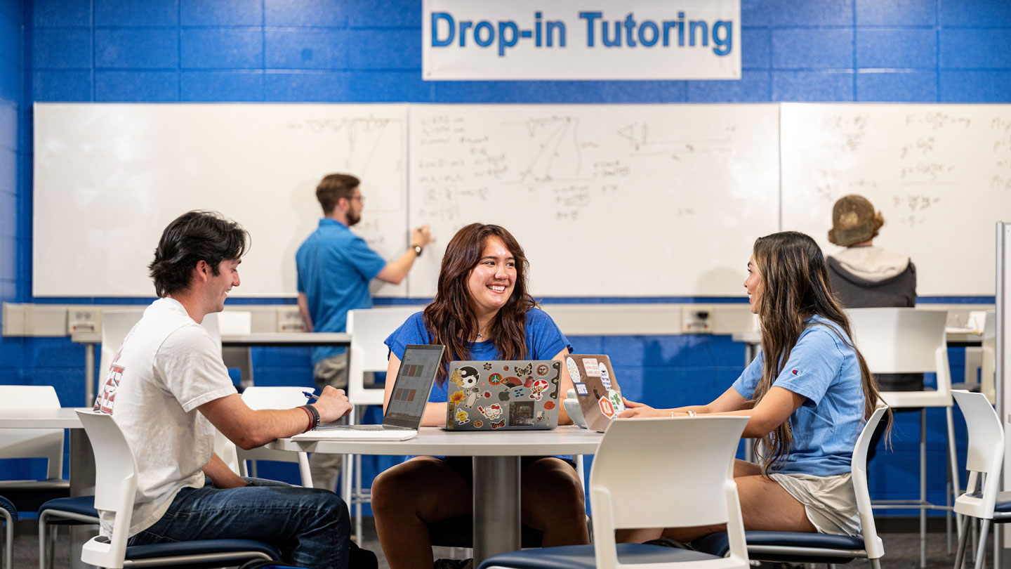 A smiling U A H tutor works with two students.