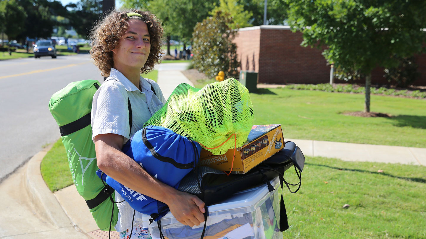 a new U A H student carries a pile of belongings into his dorm room.