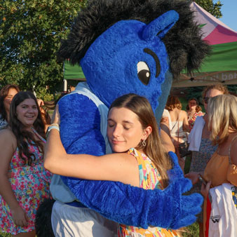 A student hugs the U A H mascot, a large blue horse