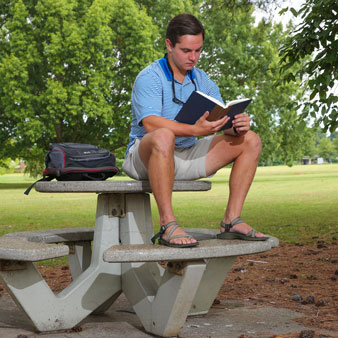 A U A H student reads a book while sitting on a picnic table