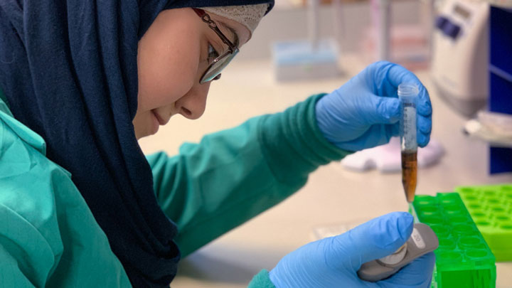 A graduate research assistant uses a pipette to transfer liquid samples into a test tube