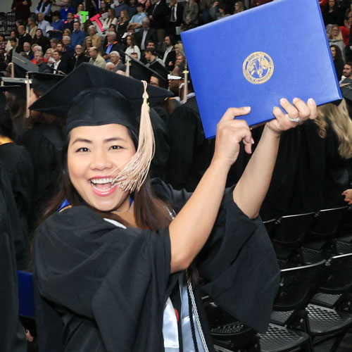 A smiling U A H student proudly displays her diploma at a graduation ceremony
