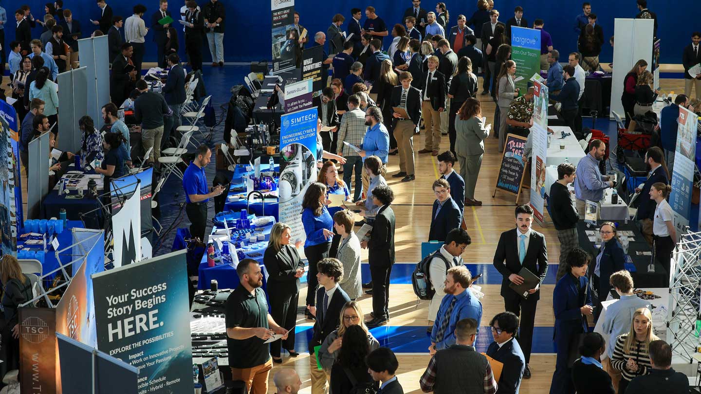 A bustling career fair showcases numerous booths and attendees engaged in networking and discussion.