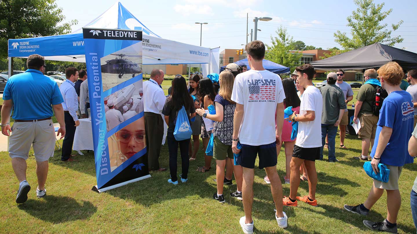 Students outside at a business booth standing in line waiting to talk to the representative.