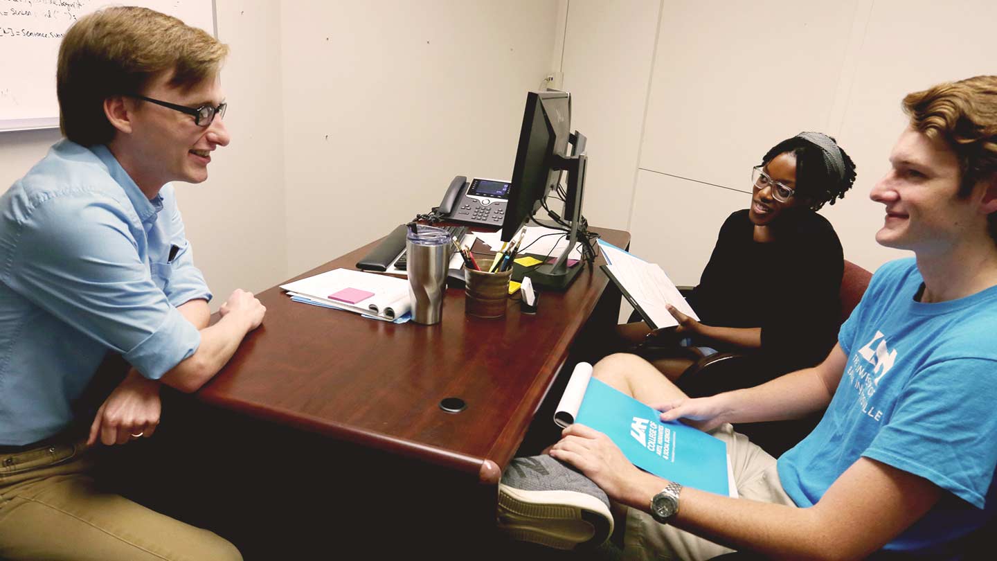 Advisor setting at desk advising two students