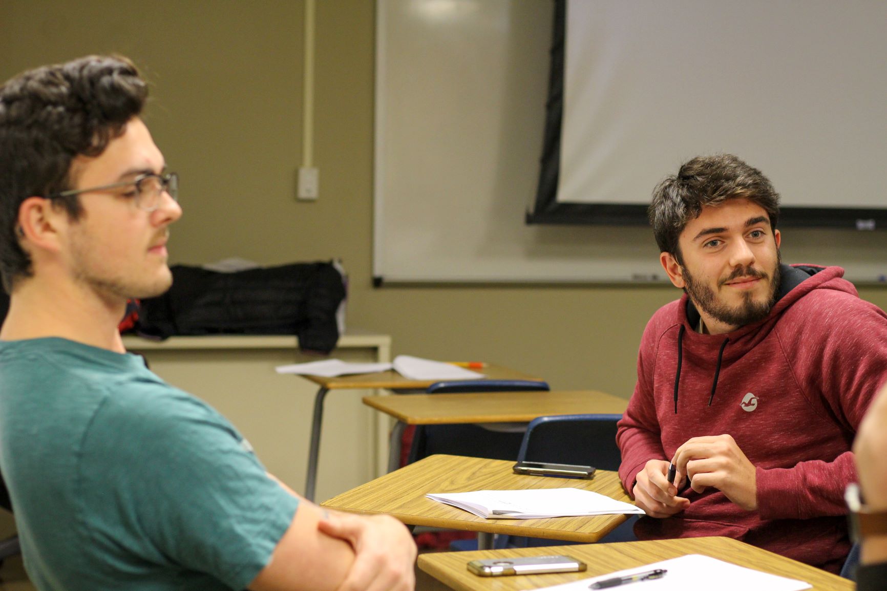 Two students setting at their desks in the classroom listenign to lecture.