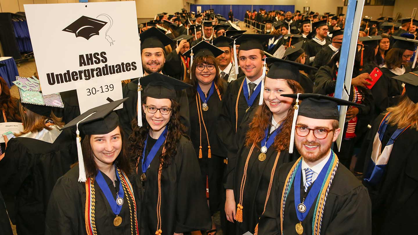 Graduates stanading for a group shot wearing caps and gowns.