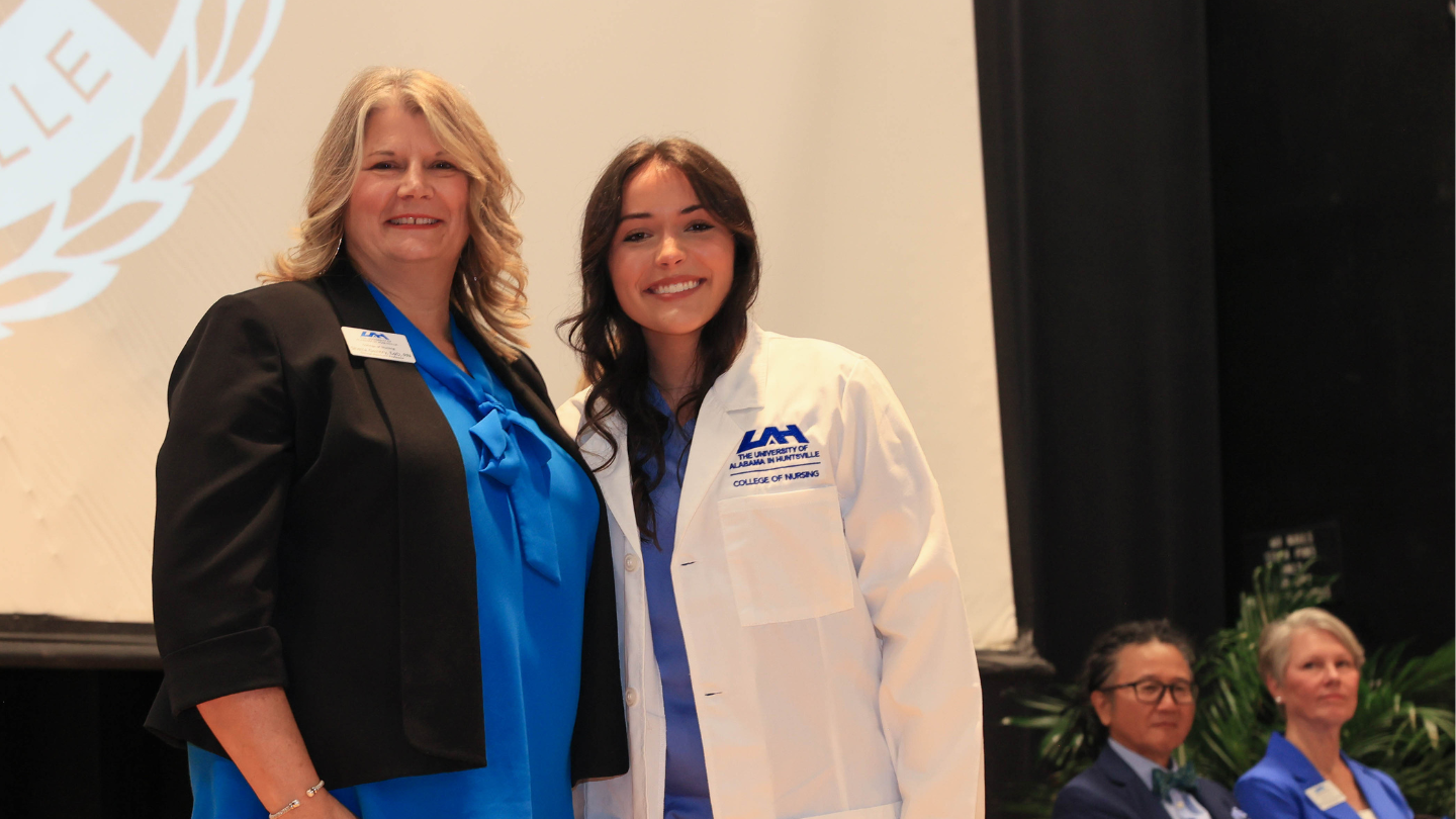 Associate Dean, Dr. Sheila Gentry in a charger blue blouse and blazer, standing to the left of Dual Nursing Student, Elizabeth Wilson in white lab coat style jacket with light blue scrubs