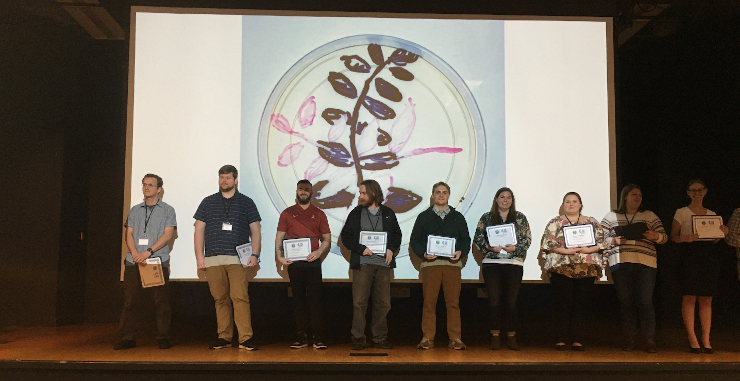 Biology award recipients standing on stage holding awards.
