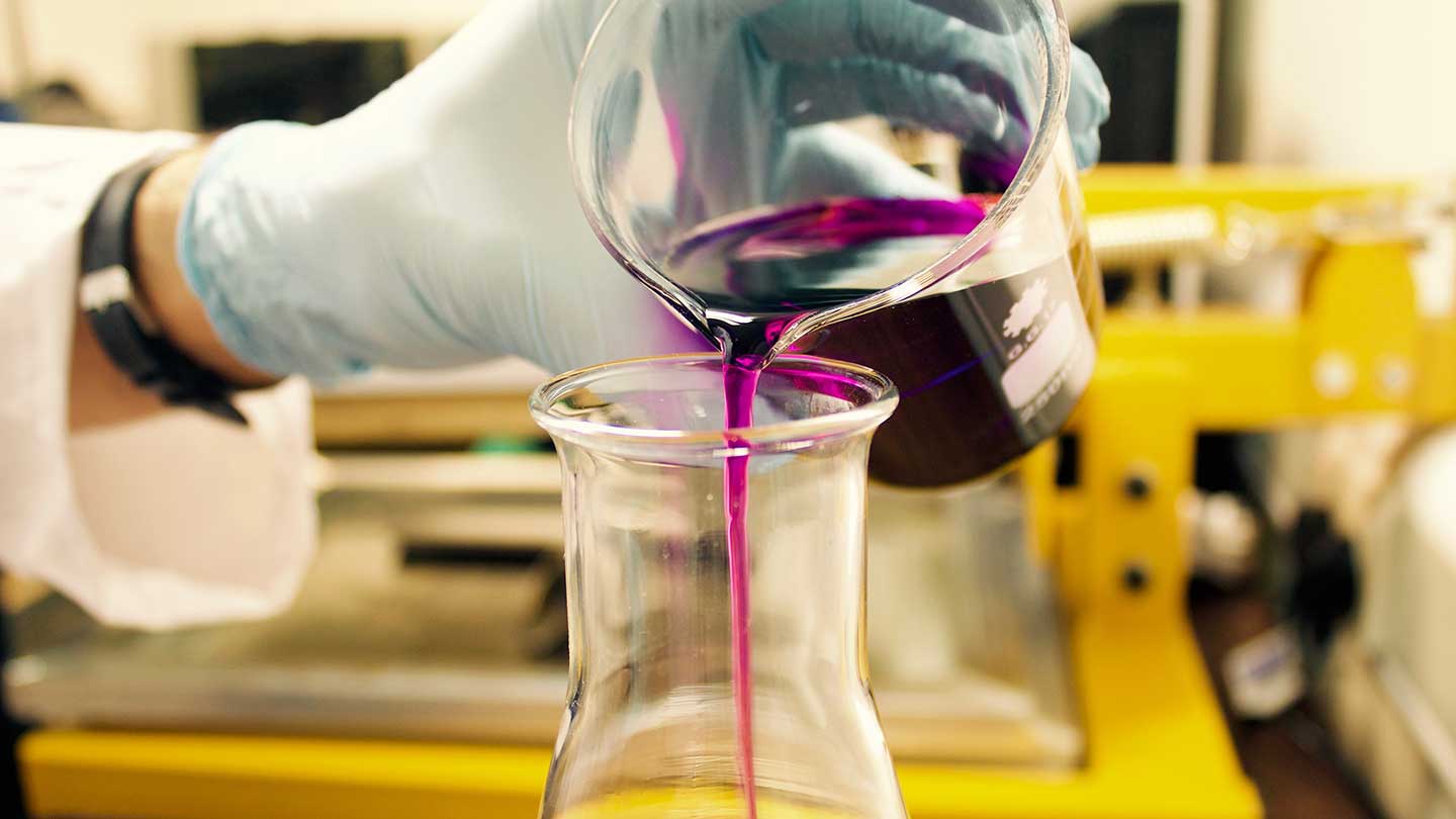 Person pouring chemicals from a beaker into a jar.