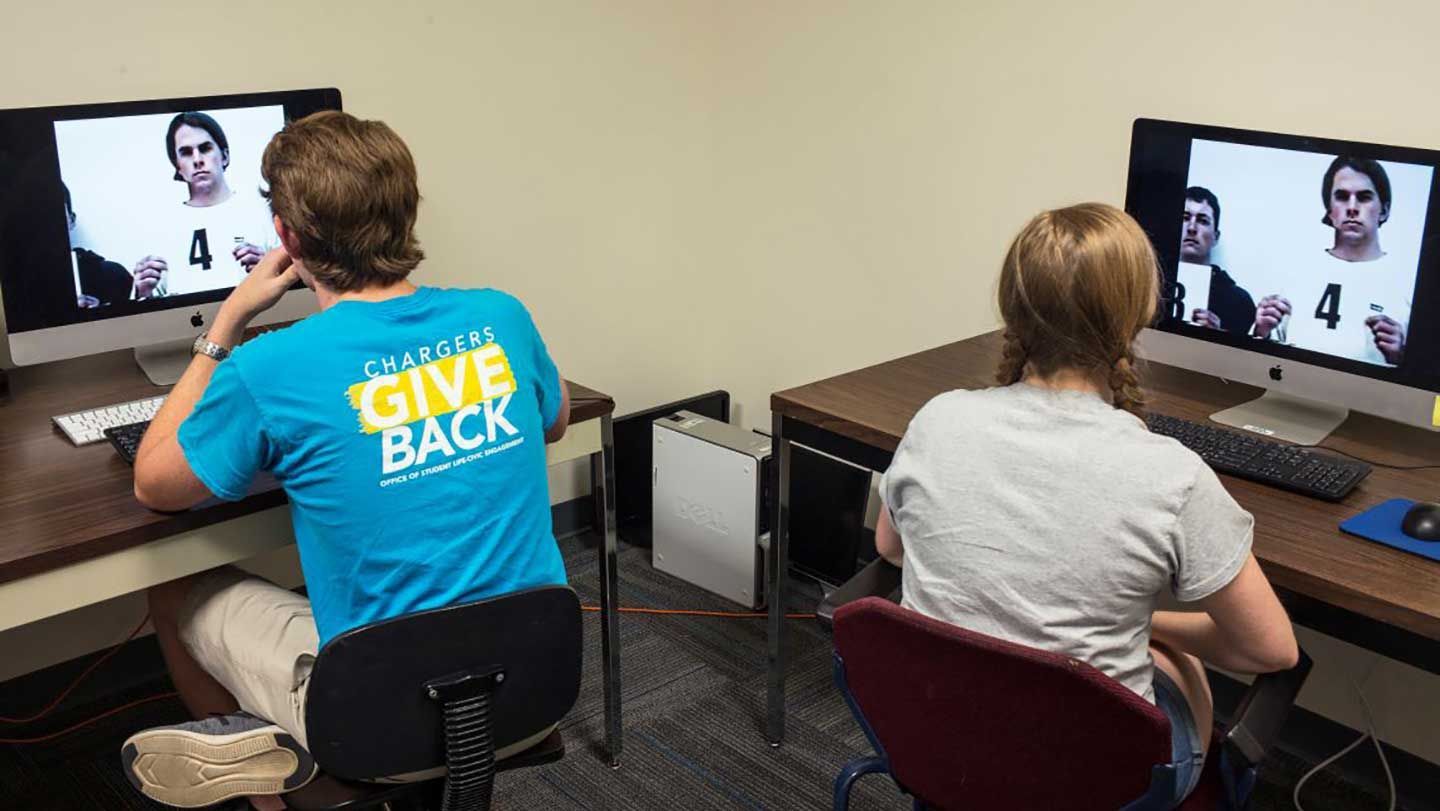 two students sit at monitors and examine a police line up photo