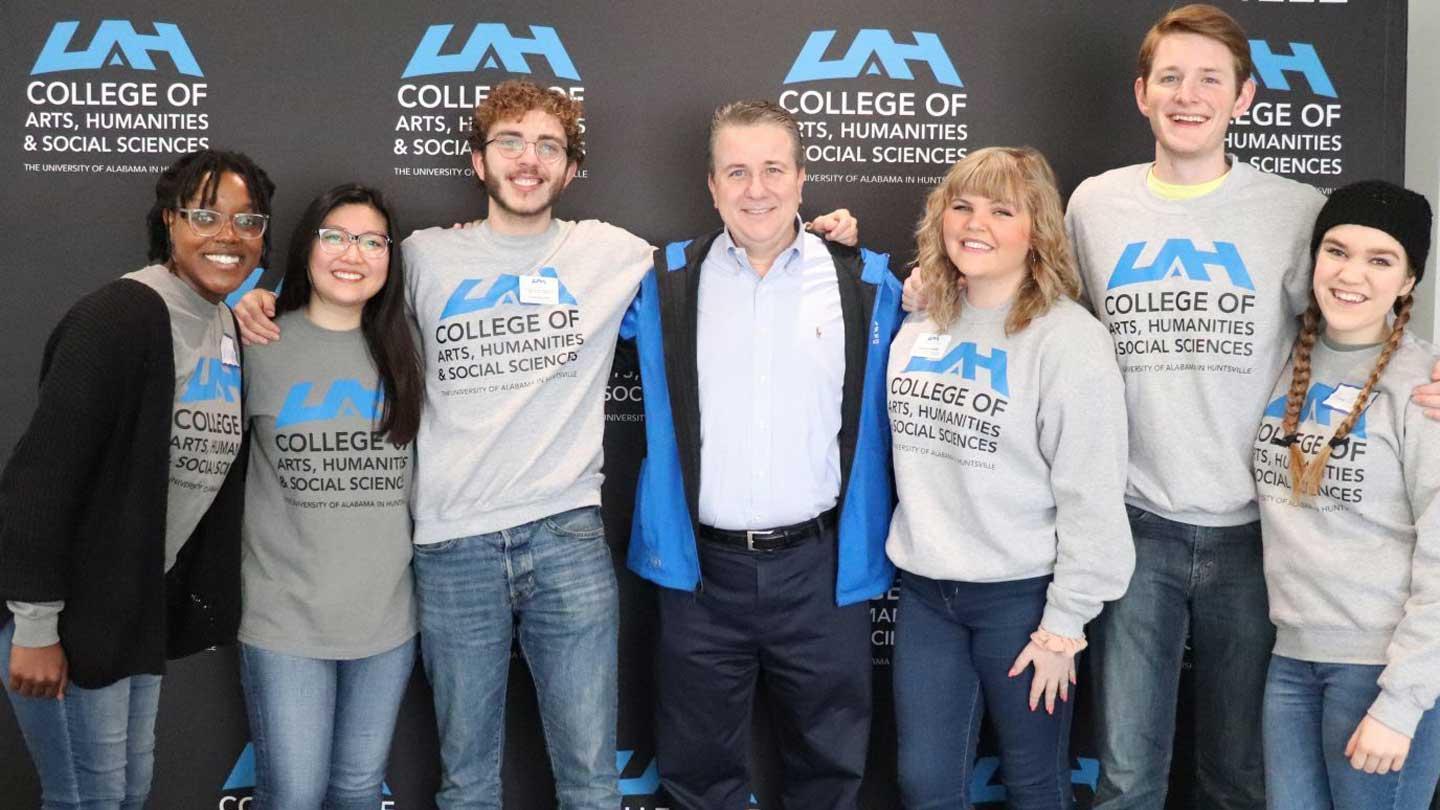 A group of seven individuals poses for a photo, wearing matching gray sweatshirts featuring the 