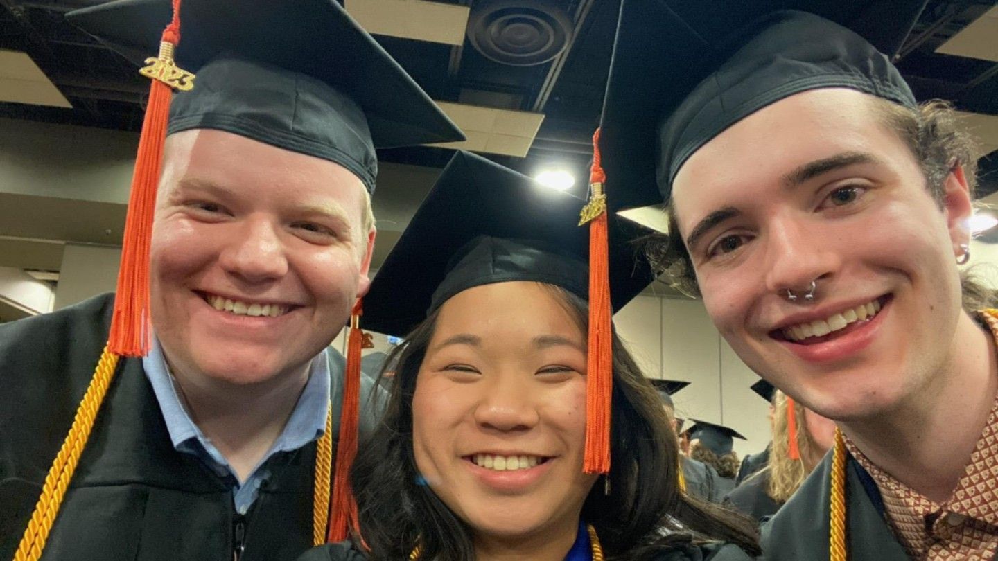 three happy people pose in cap and gown