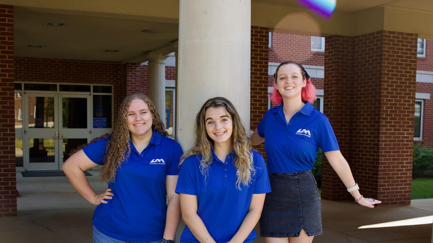 three jolly honors advisers stand happily in front of their building