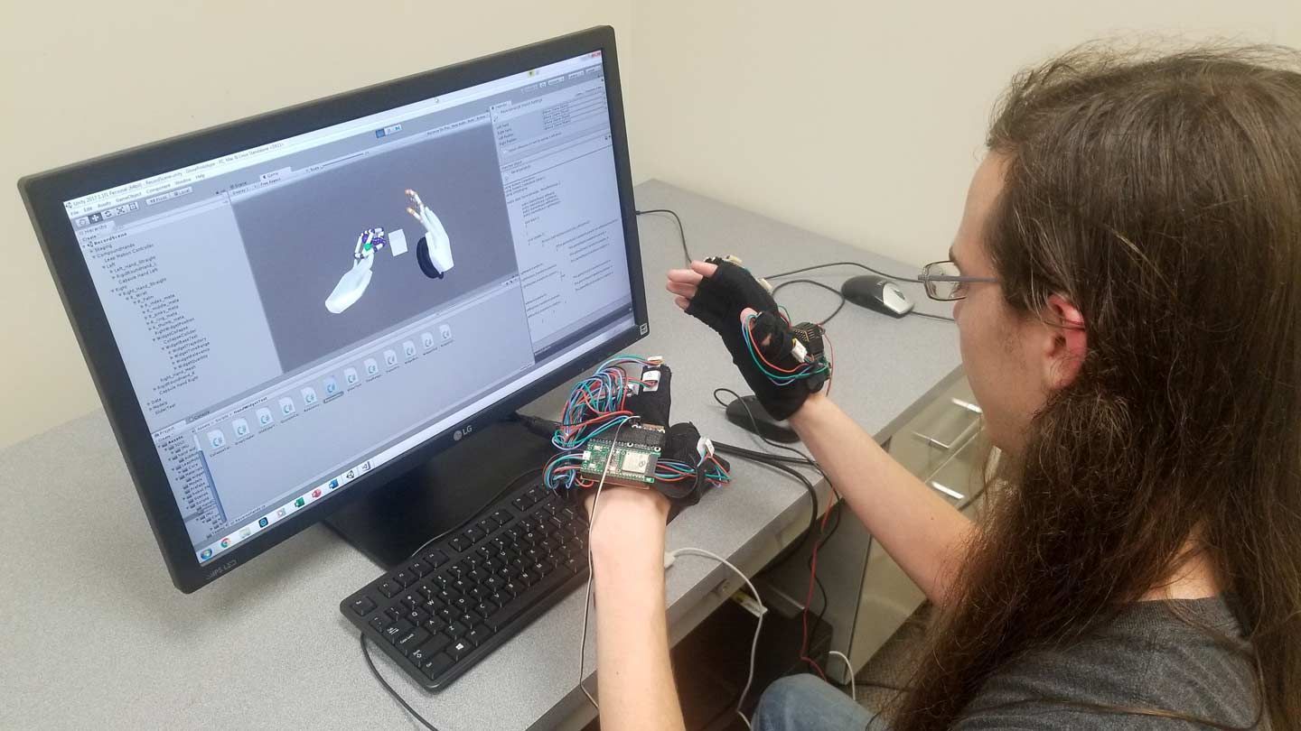 a young male college student at UAH conducts research with virtual reality gloves on a desktop computer